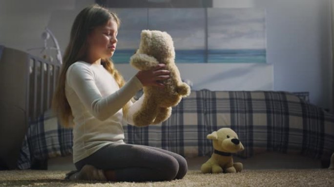 可爱的小女孩的电影镜头正在向她的泰迪熊讲述一个神奇的童话故事，并坐在托儿所舒适的地毯上拥抱它。爱情、