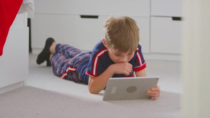 男孩在卧室里穿着睡衣看电影或躺在地板上的数字平板电脑上表演