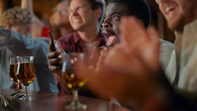 一个兴奋的年轻黑人拿着智能手机的肖像，强调了他最喜欢的足球队的体育赌注。当足球队进球时，生动的成功情