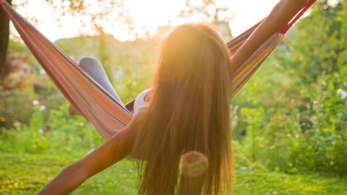 快乐的年轻女子在暑假在后院的吊床上玩得开心