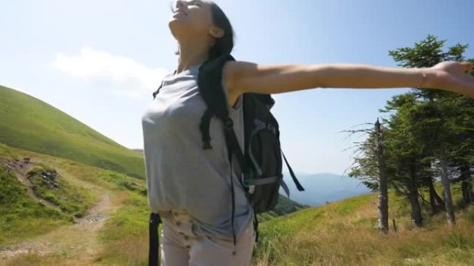 一个无忧无虑的快乐女游客背着背包，张开双臂深呼吸，在绿色自然环绕的山中徒步旅行时达到了顶峰。