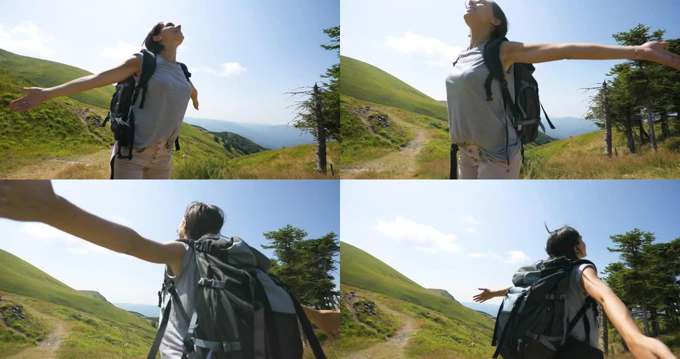 一个无忧无虑的快乐女游客背着背包，张开双臂深呼吸，在绿色自然环绕的山中徒步旅行时达到了顶峰。
