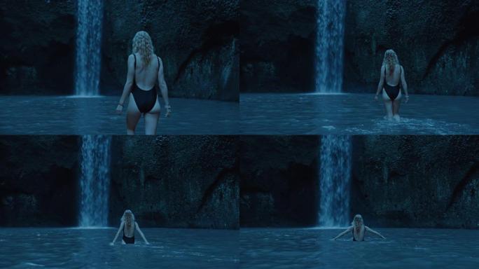 美丽的女人晚上在瀑布池里游泳，享受月光下穿着泳衣游泳的夜晚