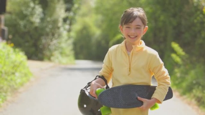 带着滑板的微笑女孩沿着乡间小路行走的肖像