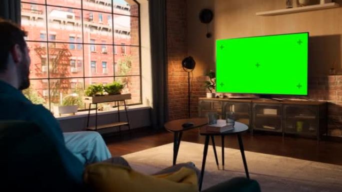 年轻的夫妇花时间在家里，坐在沙发上，在他们时尚的阁楼公寓里看绿屏模拟显示的电视。男人和女人流媒体电影