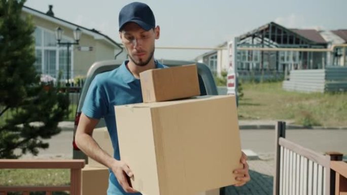 认真的年轻送货员将箱子从面包车带到郊区工作的房屋