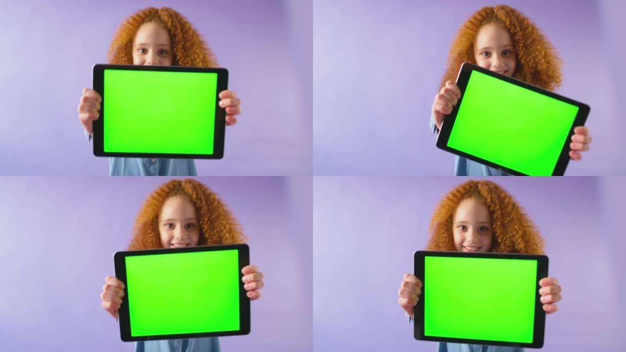 微笑女孩拿着绿屏数字平板电脑在紫色工作室背景下看着相机的工作室镜头-慢动作拍摄