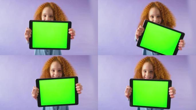 微笑女孩拿着绿屏数字平板电脑在紫色工作室背景下看着相机的工作室镜头-慢动作拍摄