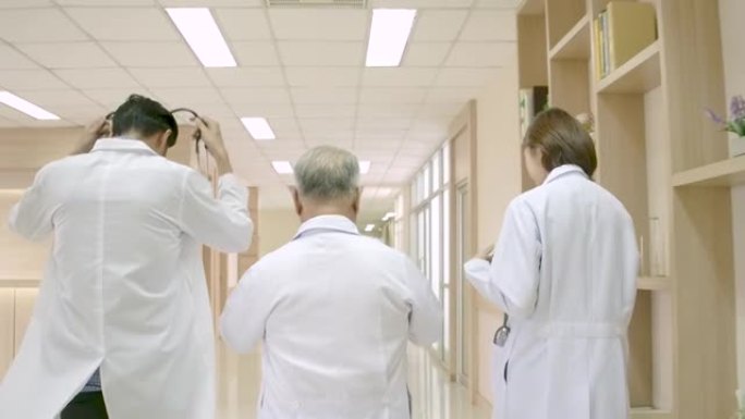 一群亚洲男女医生拿着听诊器在医院走廊里走来走去，讨论如何治疗他们的病人。医疗保健理念。