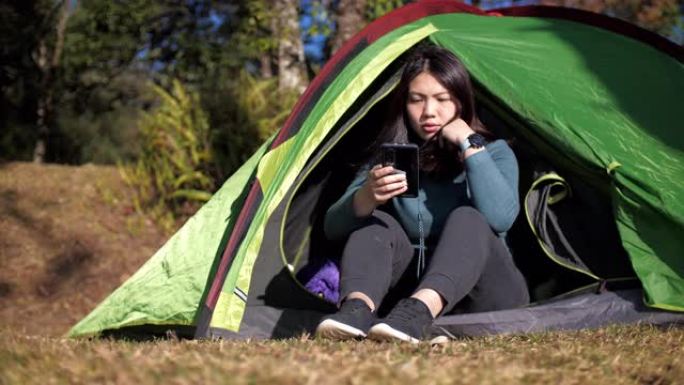 妇女在森林中的帐篷露营地使用手机