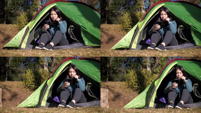 妇女在森林中的帐篷露营地使用手机