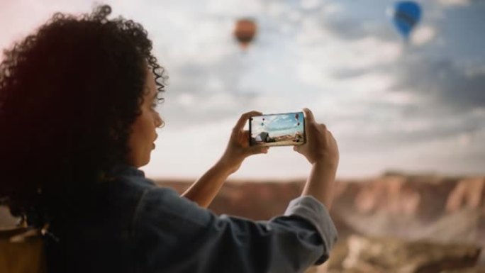 激动的年轻多民族旅行者与非洲发型拍摄的智能手机照片，美丽的大自然在岩石峡谷谷。山区国家公园的热气球节