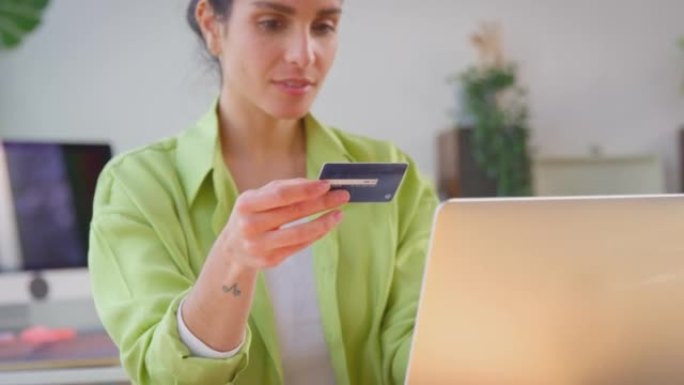 女人在家经营生意，用笔记本电脑上的信用卡在线购物-慢动作拍摄