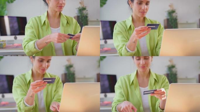 女人在家经营生意，用笔记本电脑上的信用卡在线购物-慢动作拍摄