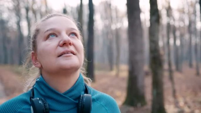 SLO MO女人在穿越秋天森林的道路上慢跑时戴上耳机