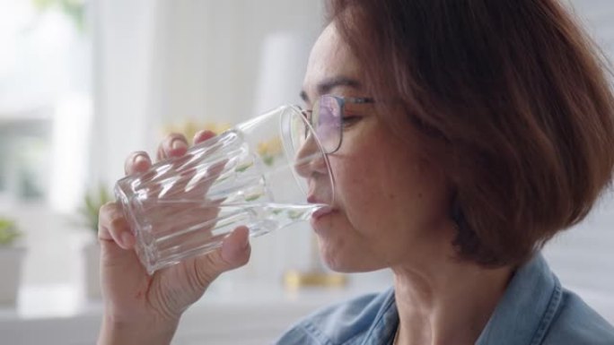 成熟的亚洲老年人在家喝水杯健康的生活方式。