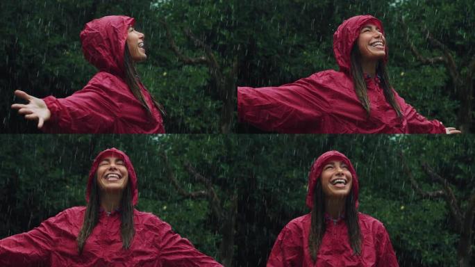 一个穿着红色雨衣的快乐女人的肖像，笑着享受在雨下。女性成年人感激水和自然的祝福，周围是树木。秋乐概念