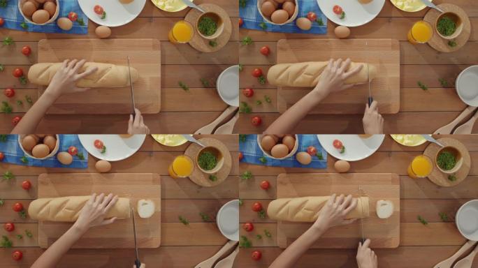 年轻的亚洲女厨师的手拿着刀子切全麦面包放在家里厨房桌子上的木板上。