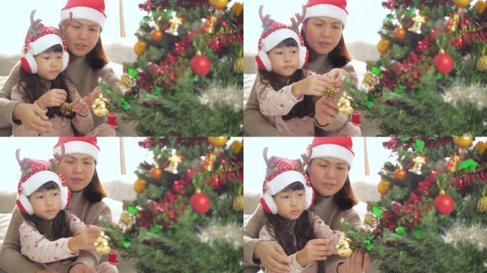 小女孩和母亲在圣诞节用装饰品装饰圣诞树