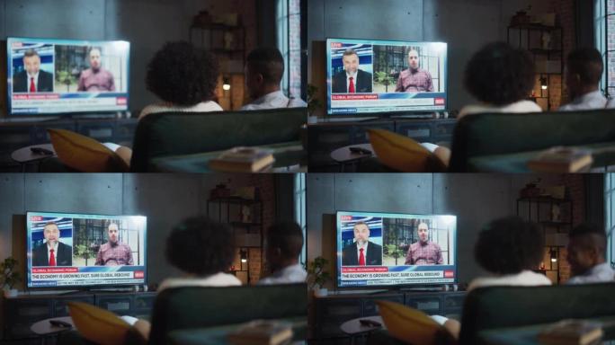黑人夫妇晚上坐在家里的沙发上看电视晚间新闻，分享他们的观点。配偶在一起。后视图镜头