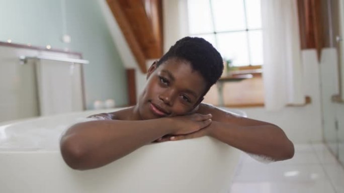 非裔美国迷人女性在泡沫浴缸中放松并在浴室中微笑的肖像