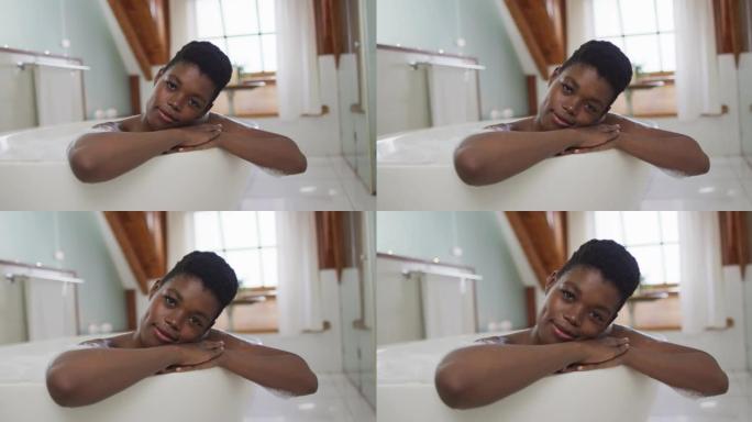 非裔美国迷人女性在泡沫浴缸中放松并在浴室中微笑的肖像