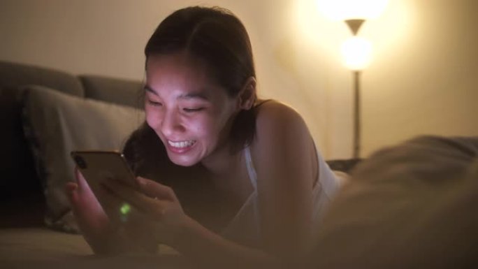 亚洲女性晚上在床上使用智能手机