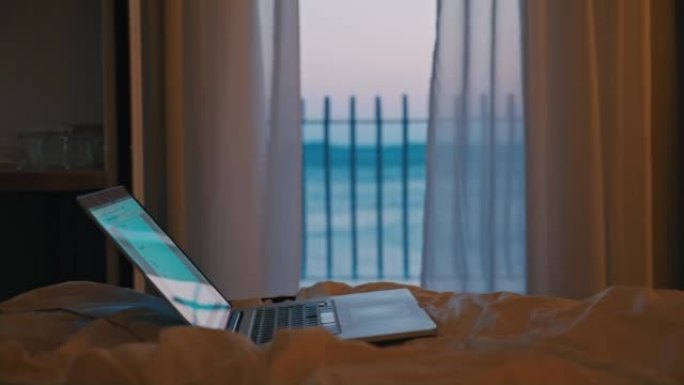 笔记本电脑站在酒店房间的床上，晚上可以看到大海，多莉运动