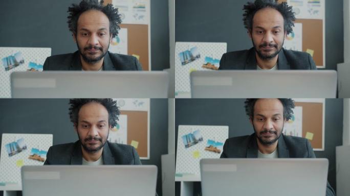 缩小阿拉伯商人的慢动作肖像，用笔记本电脑看着屏幕