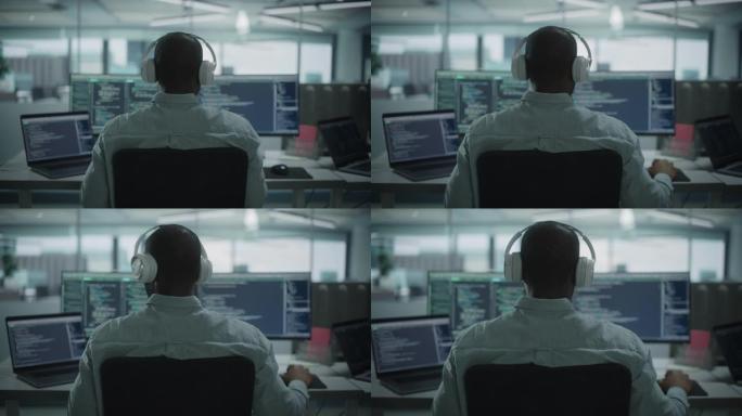 办公室: 专业的黑色IT程序员在台式电脑上工作时使用耳机。男性网站开发者，软件工程师开发应用程序，视