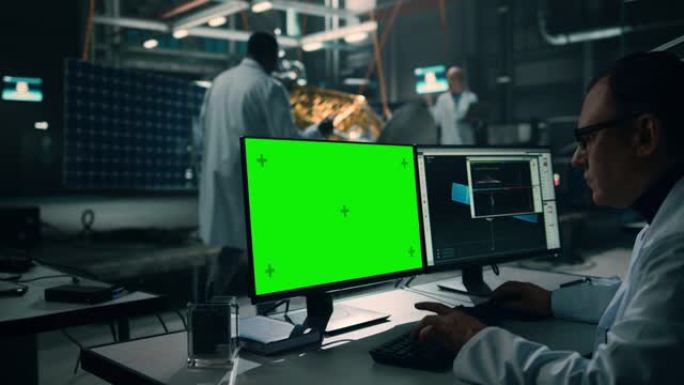 男工程师使用绿屏模拟显示计算机分析卫星。航空航天局制造设施: 科学家开发，组装用于太空探索任务的航天