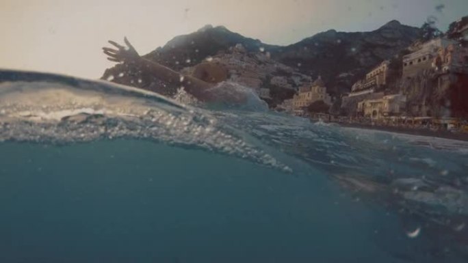SLO MO女人在一个著名的村庄Positano的海湾里游泳时，翻着湿的长发