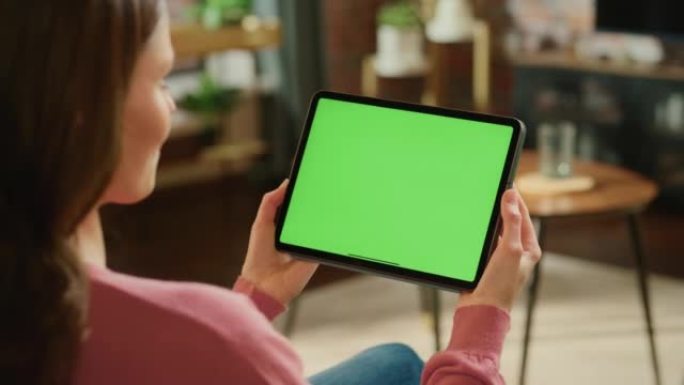 女性手持平板电脑，绿屏模拟显示。女人在家放松，在移动设备上观看视频和阅读社交媒体帖子。特写镜头。