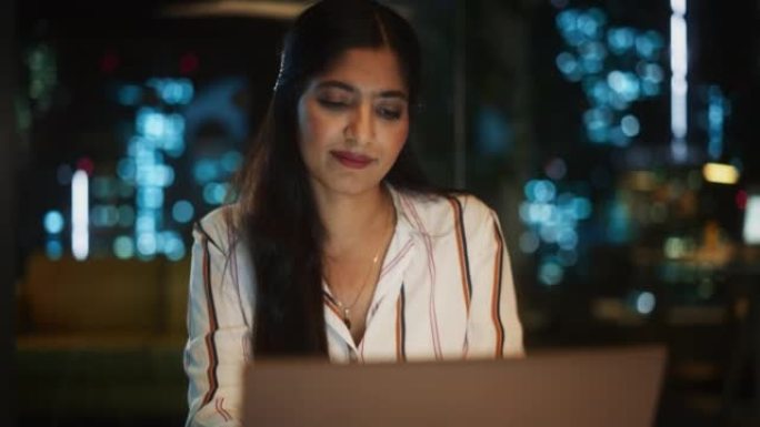 印度女性晚上在创意机构工作，为客户实施现代商业战略。成功的专家使用笔记本电脑进行认真的工作。
