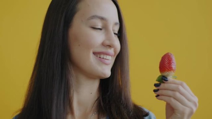 黄色背景下年轻女子拿着美味草莓微笑的特写肖像