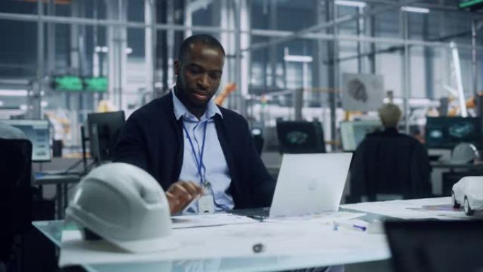 年轻的非洲裔美国工程师在汽车装配厂的办公室里使用笔记本电脑。在技术开发设施中从事车辆零件工作的工业专