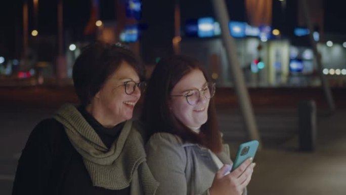 两个女人晚上在城市用手机自拍时玩得开心