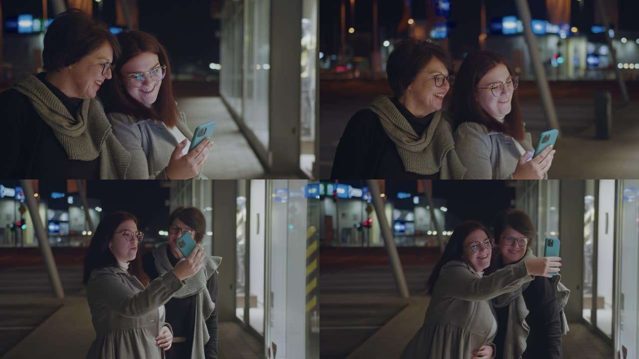 两个女人晚上在城市用手机自拍时玩得开心