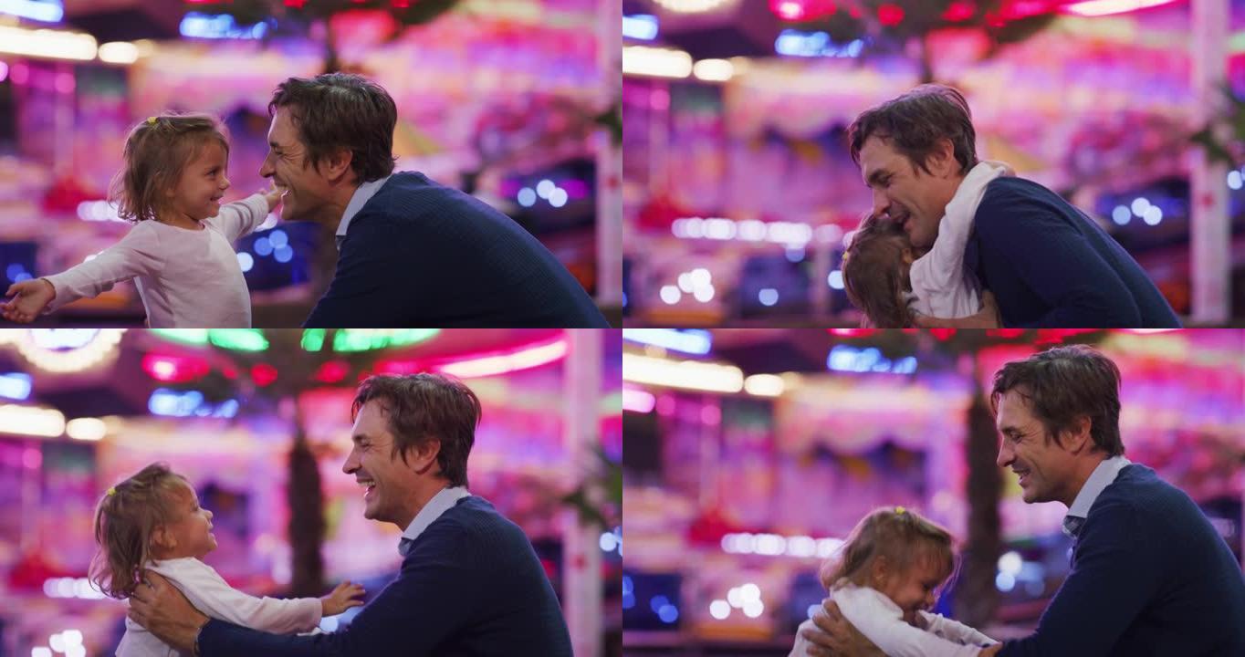 一个快乐微笑的父亲的真实镜头是深情地拥抱和亲吻他的小女儿，同时晚上在游乐园里与露娜公园的灯光一起玩耍