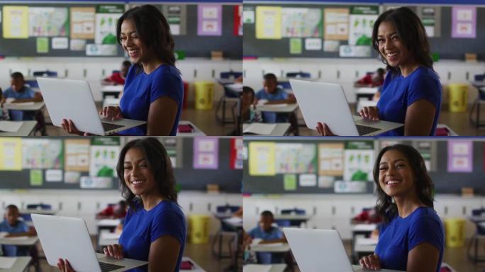 快乐混血女教师站在教室里的肖像，背景是笔记本电脑的孩子