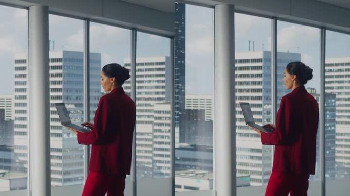 垂直屏幕。成功的女商人站在办公室时使用笔记本电脑，看着大城市的窗外。自信的女性数字企业家开发电子商务
