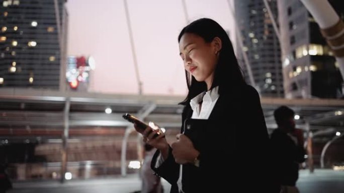 亚洲女商人晚上在城市散步和使用智能手机