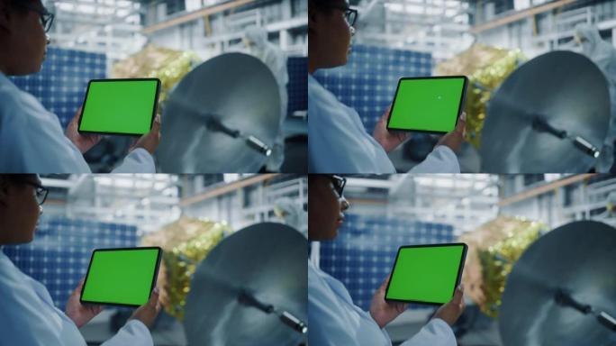 女工程师在进行卫星建设时使用绿屏数字平板电脑。航空航天局: 科学家为太空探索任务组装航天器。超过肩膀