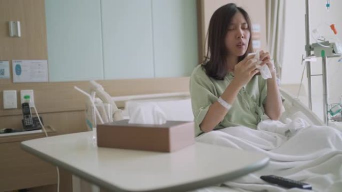 生病的亚洲病人妇女坐在床上，咳嗽和打喷嚏在医院的组织中