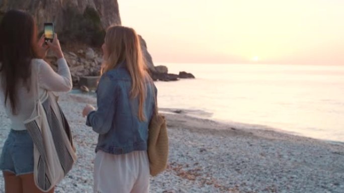 两名年轻女子一起站在沙滩上用手机拍照的4k视频