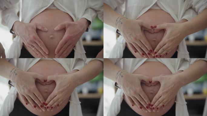 MS夫妇将他们的手以心脏的形状连接在一起，围绕着怀孕的腹部