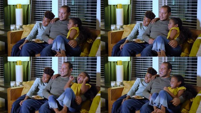 多种族的父亲，两个孩子在晚上看电视