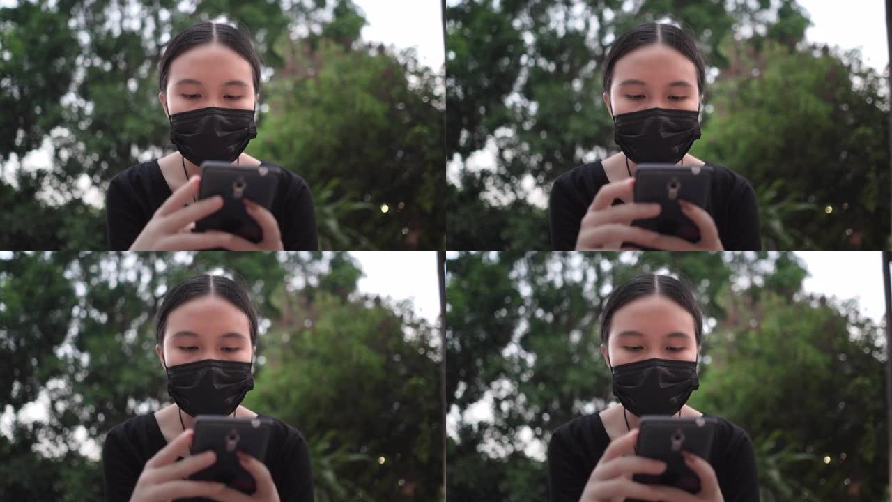 在公园里用智能手机戴口罩的亚洲少女