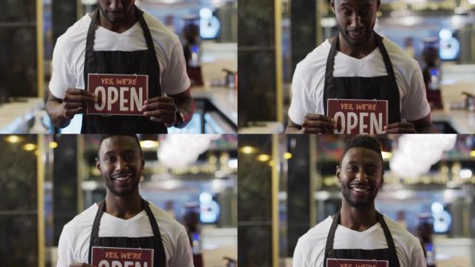 快乐的非洲裔美国咖啡师的肖像在咖啡馆里举着 “我们是开放的” 标志