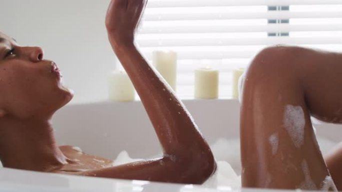 非裔美国妇女在家里浴室的浴缸里吹肥皂泡的特写